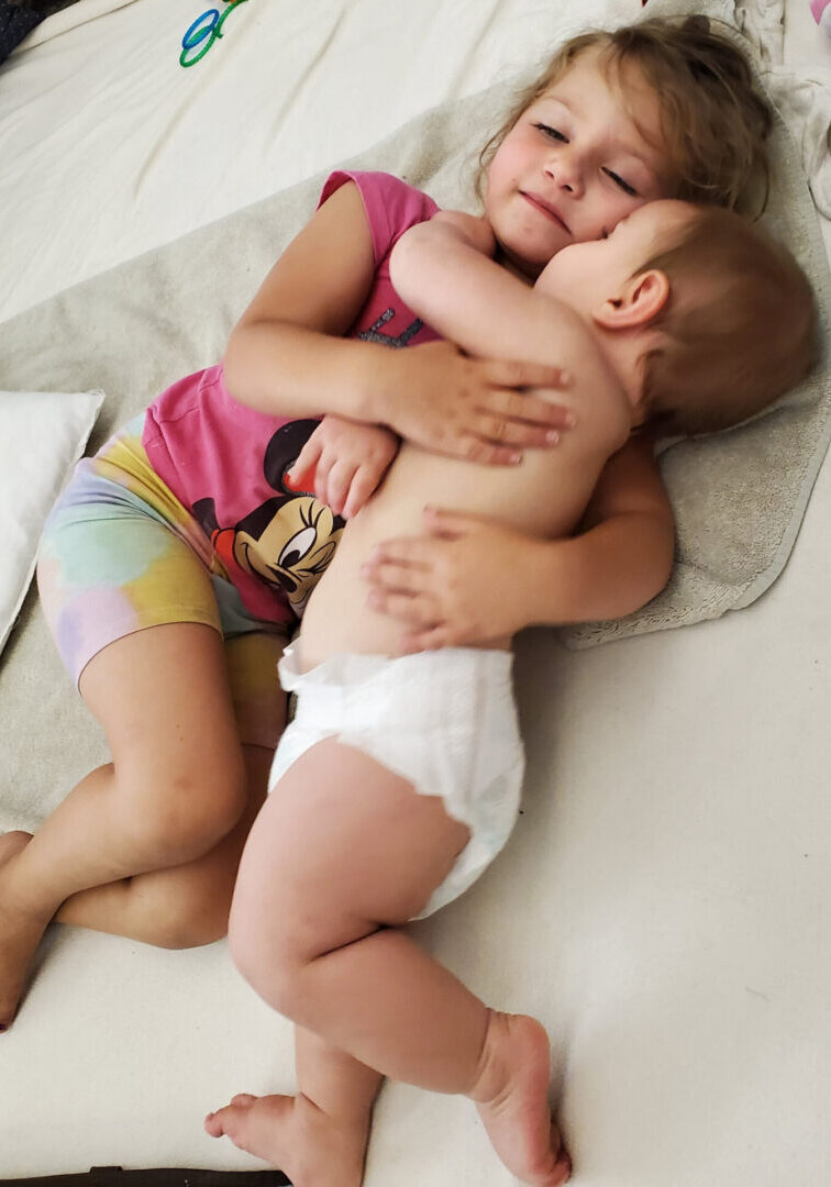 A baby is holding onto the arm of another child.